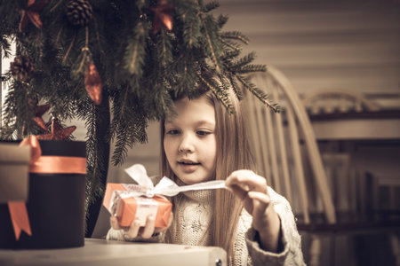 Merry Christmas, happy holidays. Cheerful cute little blonde girl opens a Christmas present.の写真素材