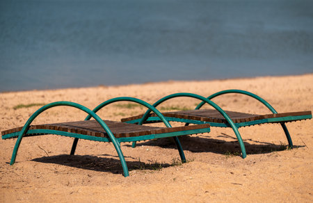 Two metal deck chairs stand on a sandy beach against the backdrop of the sea.