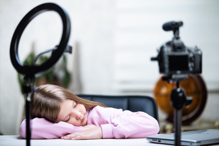 Beautiful blonde teen live streaming, tired and fell asleep. The video blogger is broadcasting live. Ring lamp and camera during the live broadcast of a vloggerの写真素材