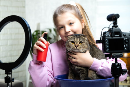 A beautiful blonde teen is live streaming with a cat, a pet. The video blogger is broadcasting live. Ring lamp and camera during the live broadcast of a vloggerの写真素材