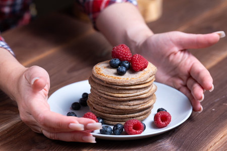 A stack of pancakes with fresh raspberries and blueberries on a light plate on a wooden backgroundの写真素材