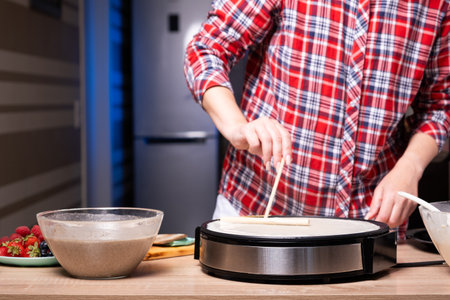 Woman cooking delicious crepe on electric pancake maker in kitchen, closeup.の写真素材