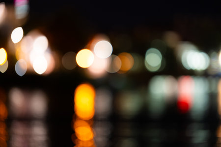 Blurred background of a night city and a body of water. Bright glowing lights of an area in a metropolis under a twilight sky in the evening on a blurred background.の写真素材