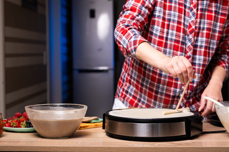 Woman cooking delicious crepe on electric pancake maker in kitchen, closeupの写真素材