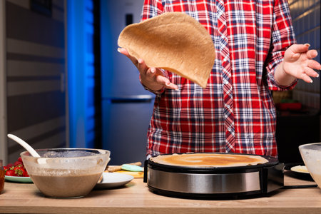 Woman cooking delicious crepe on electric pancake maker in kitchen, closeup.の写真素材