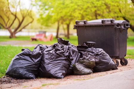 A pile of plastic garbage bags on the side of the road near a plastic container. Garbage bags on the...