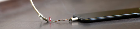 The smartphone is charging from a faulty cable. The concept of danger, the use of non-standard equipment, worn-out equipmentの写真素材