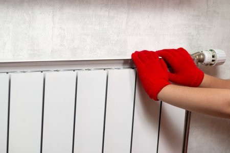 Hands in red gloves on a white radiator. Central heating radiator at home.の写真素材