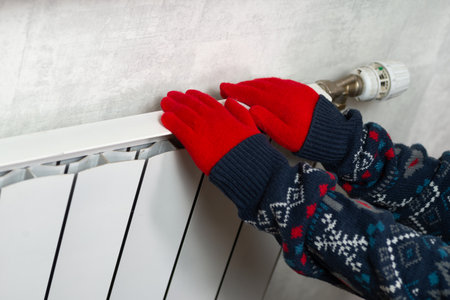 Hands in gloves on a radiator. Central heating radiator at home. A child in woolen gloves warms his hands near the heaterの写真素材