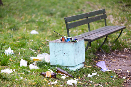 A trash can is positioned right next to a bench that is located in a park