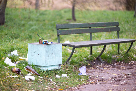 A trash can is positioned right next to a bench that is located in a parkの写真素材