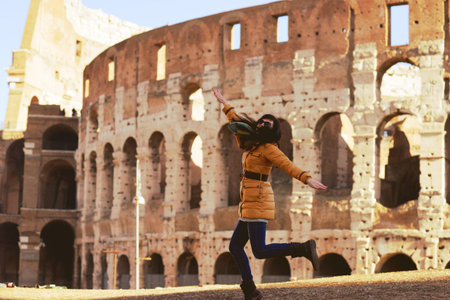 Young woman in winter clothes having fun on the background of the Winter Colosseum in Rome. The girl...