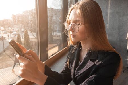 Young woman at cafe drinking coffee and using mobile phoneの写真素材