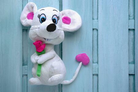 soft toy white rat with a purple rose on a light blue wooden background with blur for the holiday on March 8 or February 14の写真素材