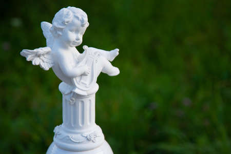 figurine angel playing the harp on a green background with blurの写真素材