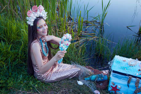 young girl with long hair in a crown of seashells trying on beadsの写真素材