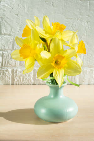 yellow daffodils in a turquoise vase against a white brick background with a ripple verticallyの写真素材