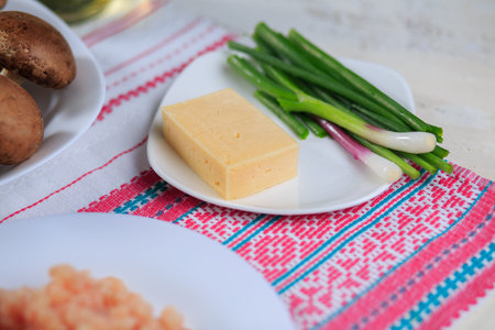 Firm cheese and green onions on a white plate on a light background