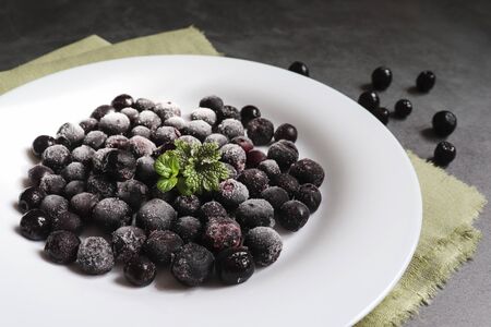 Frozen fruit. Frozen black rowan berries on a white plate and cement background. The concept of the use and preservation of frozen foods.の写真素材