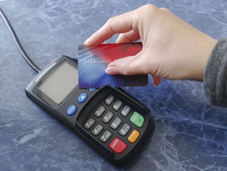 The female hand holds a credit card on the payment terminal. Cashier machine to withdrawals money. Nfc technology. Finance and cashless way to pay for purchase. Contactless payment conceptの写真素材