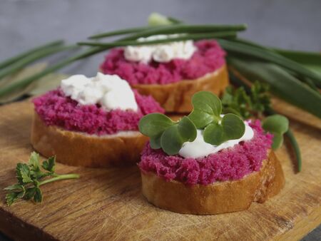 Bright beetroot hummus on a slice of bruschetta with sauce and microgreen on an aged wooden board. Festive appetizer, vegetarian food, sandwiches. Vegan.の写真素材