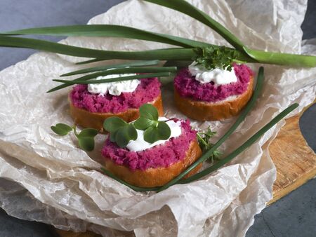 Beetroot hummus on a sliced baguette with sauce, parsley and green onions and microgreen on paper. selective focus Festive snack, vegetarian food, sandwiches. Healthy eatingの写真素材