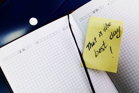 Top view of an open notebook with motivational note. This is the best day. Business concept. Yellow sticker. Notepad with a bookmark. Optimistic record. Motivation for action.の写真素材