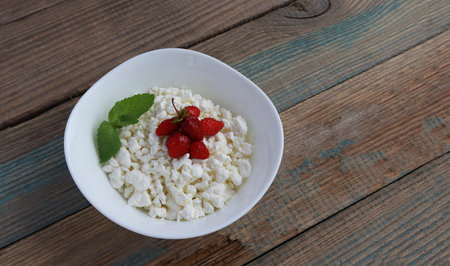 cottage cheese . fresh diet curd homemade in a white plate with ripe strawberries and mint leaf on...