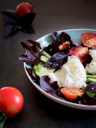 plate with poached egg, fresh tomatoes, cucumber, purple lettuce leaves on a dark background.