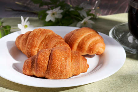 Fresh baked croissants lie on a white plate. Warm fresh croissants and butter rolls. French and American croissants and pastries are popular all over the world for breakfast.の写真素材