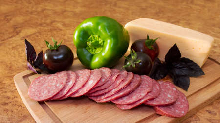 sausage with vegetables dark tomatoes, peppers, basil and cheese on a wooden cutting board. selective focus. the concept of rustic food.の写真素材