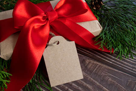 A box with a red bow and a tag for your text on a wooden background. can be used as a mockup for sale and discountsの写真素材
