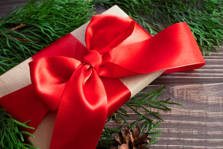 A gift with a red bow close-up on a wooden background among the green branches of the Christmas tree.の写真素材