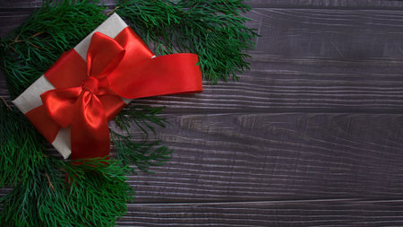 A boxwith a gift and a red bow of ribbon on a wooden background. Banner. Place for your text, copy...