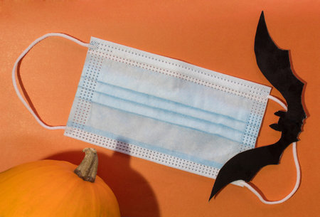Halloween during the COVID-19 coronavirus pandemic. Medical mask on an orange background, bat decor....