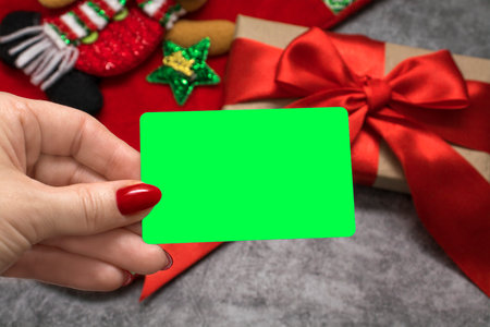 The woman's hand holds a white card with a place for text against the background of a gift with a red bow. mock up. copy space. concept of holiday discounts and online shopping. Green Screen, Chroma key,の写真素材
