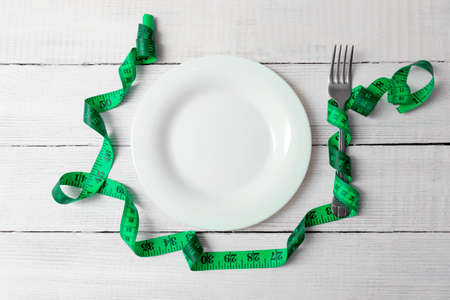 Diet Concept. Slimming and weigh loss concept. Empty plate on a wooden table with a fork and a centimeter ribbon. A place for text.の写真素材