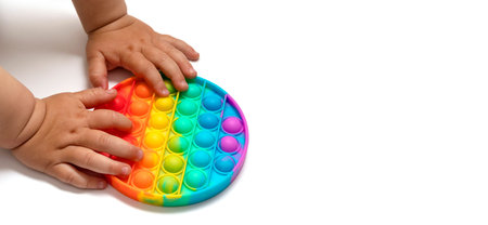 The baby's hands hold the toy anti-stress drink. The child plays with the popular pop toy it. A white background with a place for text. A copyspace.の写真素材