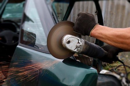 Men's hands in a glove saw a grinding machine with a trimmed disc of a car with the formation of...