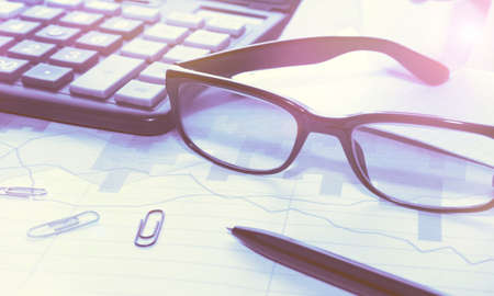Workplace in the office of a businessman, accountant, economist at prices. Glasses, calculator and pen, business documents, graph of financial charts. Business concept. Toning, soft selective focus.の写真素材
