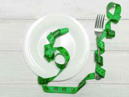 Measuring tape on a white empty plate on the table, next to the fork. The concept of weight loss, diet, slimmingの写真素材