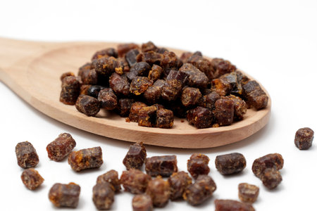 Granules of beer bread in a wooden spoon on a white background. Bee pollen Natural remedy for...