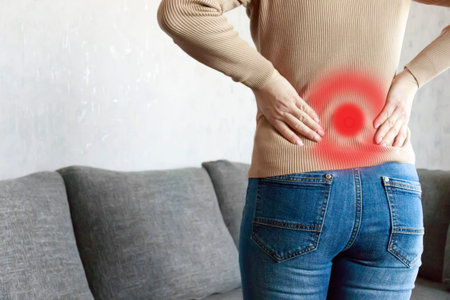chronic back pain. Adult woman is holding her lower back, while standing and suffering from...