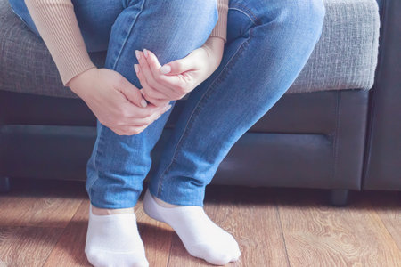Woman sitting on the couch, holding her ankle injury, feeling pain. Health care and medical concept....