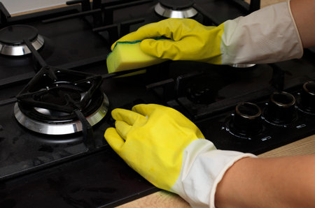 Hand in a yellow glove washes the stove. Hand washing gas stove with sponge, house cleaning concept.