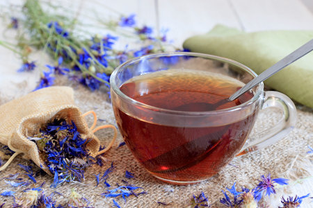 A cup of tea with cornflowers is on a wooden table. Dried meadow herbs and herbal tea on old wooden table. fresh medicinal plants and bundle. Preparing medicinal plants for health promotion. high quality photoの写真素材