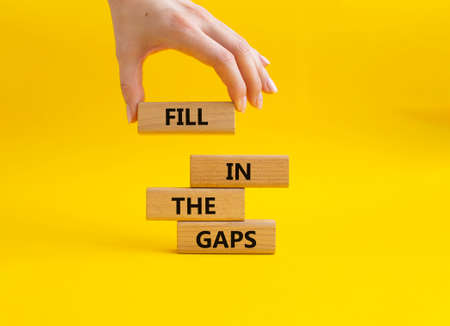 Fill in the gaps symbol. Concept words fill in the gaps on wooden blocks. Beautiful yellow background. Businessman hand. Business and fill in the gaps concept. Copy space.の写真素材