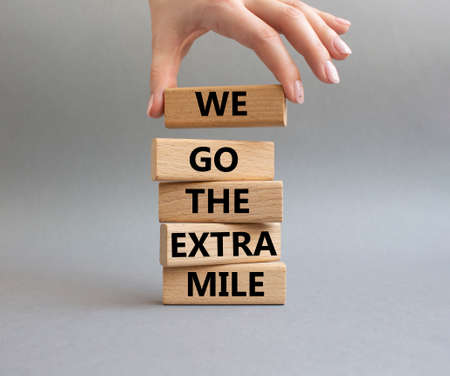 We go the extra mile symbol. Wooden blocks with words 'We go the extra mile'. Beautiful grey background. Businessman hand. Business and 'We go the extra mile' concept. Copy space.の写真素材