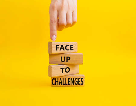 Face up to challenges symbol. Wooden blocks with words Face up to challenges. Beautiful yellow background. Businessman hand. Business and Face up to challenges concept. Copy space.の写真素材