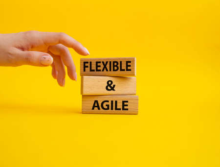 flexible and agile symbol. Concept word Flexible and agile on wooden blocks. Beautiful yellow background. businessman hand. Business and flexible and agile concept. copy spaceの写真素材